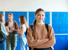 A girl smiles confidently at the camera in a school locker room.