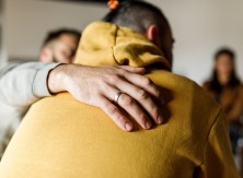 A man comforts another man by placing a hand on his back.