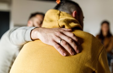 A man comforts another man by placing a hand on his back.