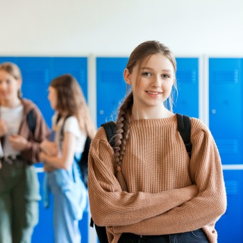 A girl smiles confidently at the camera in a school locker room.