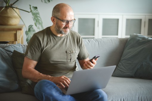 A middle aged man looks at his laptop and phone. 