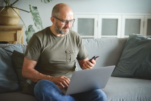 A middle aged man looks at his laptop and phone.