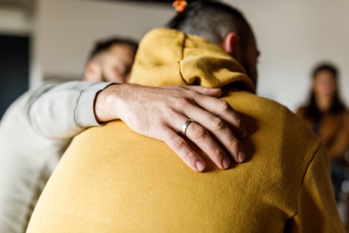 A man comforts another man by placing a hand on his back.