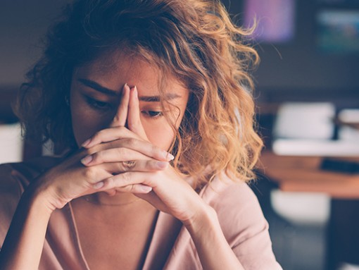 Woman sitting at table with her hands crossed in front of her face